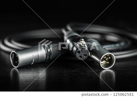 Xlr connectors and audio cable lying on a dark wooden surface 125062581