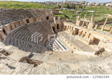 Stone seating and stage of jerash roman theatre with modern city in background 125062584