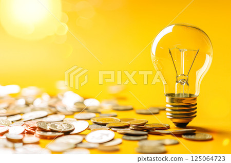 Light bulb is surrounded by a pile of coins Light bulb is surrounded by a pile of coins 125064723