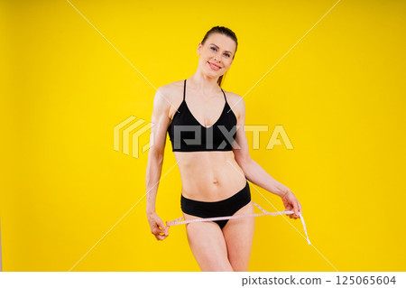 Smiling slim woman measuring her waist with tape. Fit young lady perfect shape, happy with her body Smiling slim woman measuring her waist with tape. Fit young lady perfect shape, happy with her body 125065604
