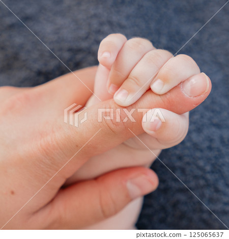 Close-up image of a babys hand tightly gripping an adults finger, symbolizing love, connection, and nurturing. Captures the essence of familial bonds and tender moments. 125065637