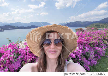 Portrait of a female traveler in sunglasses and a straw hat taking selfies against the backdrop of Thailand's nature, Cheo Lan Lake in Khao Sok Park. Tourism and solo travel 125066077