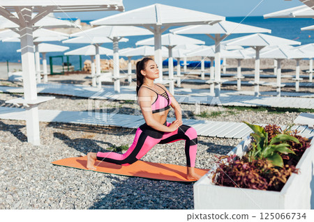 woman in tracksuit doing gymnastics yoga asana on the beach by the sea woman in tracksuit doing gymnastics yoga asana on the beach by the sea 125066734