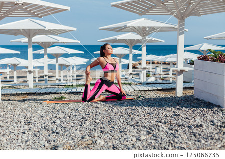 brunette does sports gymnastics yoga asana on the beach by the sea brunette does sports gymnastics yoga asana on the beach by the sea 125066735