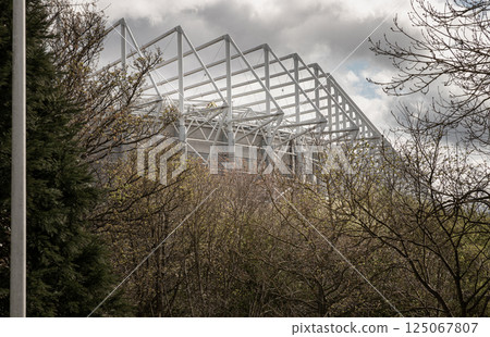 Look up through the bushes in a park at the steel structure of St James' Park stadium. 125067807