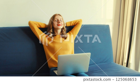 Happy young woman relaxes while working on laptop, freelancer girl enjoys free time sitting at home Happy young woman relaxes while working on laptop, freelancer girl enjoys free time sitting at home 125068653