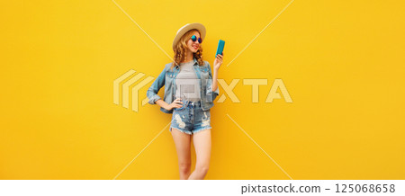 Summer stylish happy young woman with smartphone in straw tourist hat posing on yellow background 125068658