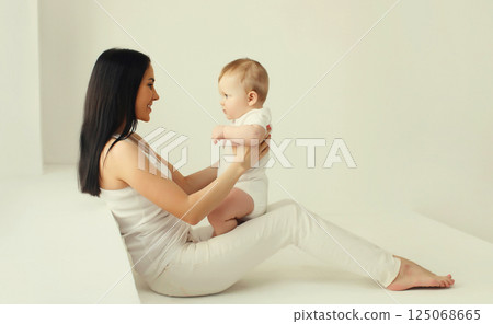 Happy smiling young mother playing with baby in white room at home Happy smiling young mother playing with baby in white room at home 125068665