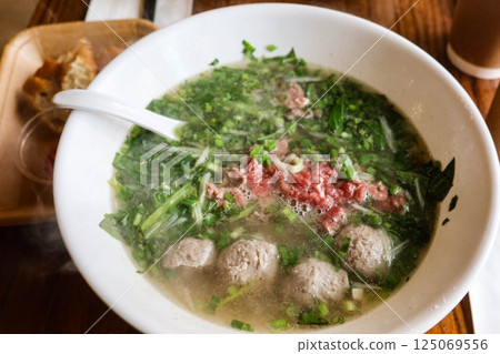 close up of Vietnamese beef pho rice noodles with beef ball and thinly sliced raw beef added to a steaming bowl of savoy broth close up of Vietnamese beef pho rice noodles with beef ball and thinly sliced raw beef added to a steaming bowl of savoy broth 125069556