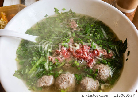 close up of Vietnamese beef pho rice noodles with beef ball and thinly sliced raw beef added to a steaming bowl of savoy broth 125069557