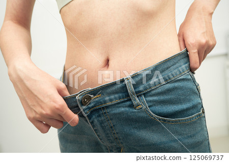 Young Asian woman losing weight wearing loose pants in oversize jeans. 125069737
