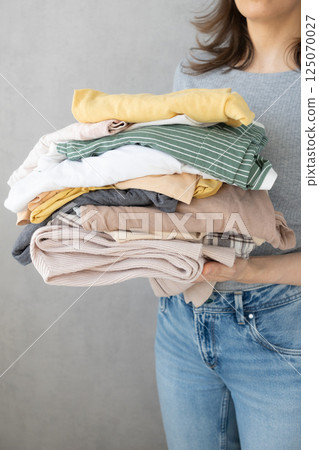 Laundry, woman holds stack of clothes in her hands after dry cleaning. housework, cleaning ironing.  125070027