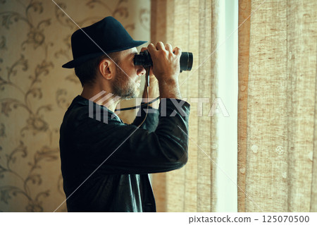 Man in fedora hat looking through binoculars spying from window Man in fedora hat looking through binoculars spying from window 125070500