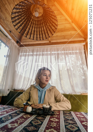 Woman in a Tan Jacket Enjoying Coffee in a Cozy Cafe Woman in a Tan Jacket Enjoying Coffee in a Cozy Cafe 125071231