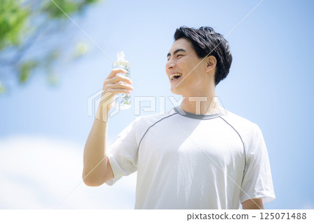 Close-up of a young man hydrating (drinking water) during running sports or exercise under blue sky Close-up of a young man hydrating (drinking water) during running sports or exercise under blue sky 125071488