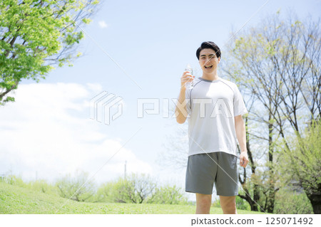 A young man hydrating (drinking water) during running sports or exercise under a blue sky A young man hydrating (drinking water) during running sports or exercise under a blue sky 125071492