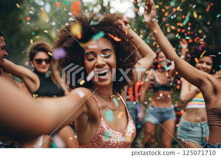 Young woman with afro hairstyle laughing and dancing with friends at a music festival with confetti falling 125071710