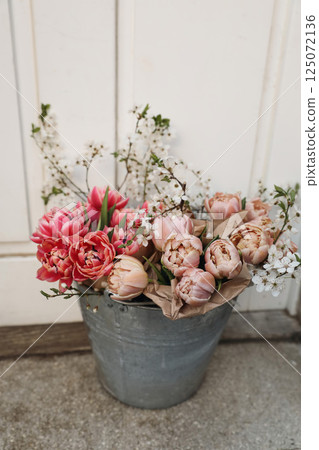 Feminine spring Easter still life. Pink tulip flowers, blooming cherry plum tree branches in metal bucket. Blurred wooden front door background. Floral birthday wedding decoration. Vertical. Top view. 125072136