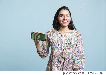 Confident woman presenting green screen on mobile gadget, standing against studio background. Cheerful indian person holding copy space chroma key smartphone used for advertising brands. Confident woman presenting green screen on mobile gadget, standing against studio background. Cheerful indian person holding copy space chroma key smartphone used for advertising brands. 125072182