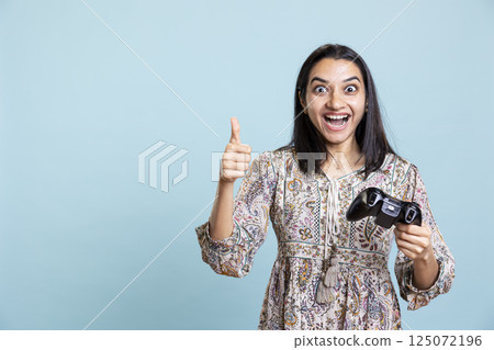 Indian girl winning the video game championship and giving thumbs up, feeling confident and happy with her victory. Ecstatic jolly woman entertained by video games on the console. 125072196