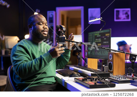 Talented young artist performing an acoustic version of his new song, reading the lyrics on his smartphone. Professional musician producing a new track, recording audio files on microphone. 125072268