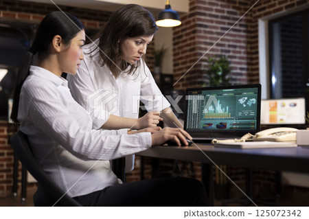 A professional discussion between coworkers, collaborating on a business project, using research data on laptop. White woman stands and reviews details as her colleagues scrolls through the document. A professional discussion between coworkers, collaborating on a business project, using research data on laptop. White woman stands and reviews details as her colleagues scrolls through the document. 125072342