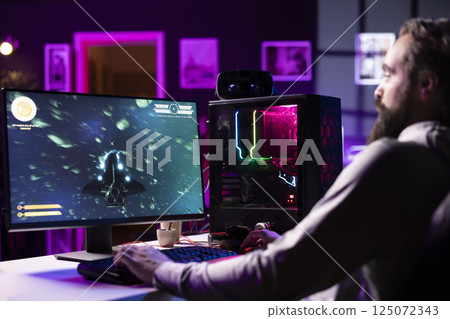Man having fun by using gaming keyboard to fly spaceship in SF videogame, unwinding at home. Gamer using powerful PC and computer peripherals to play game, entertaining himself Man having fun by using gaming keyboard to fly spaceship in SF videogame, unwinding at home. Gamer using powerful PC and computer peripherals to play game, entertaining himself 125072343