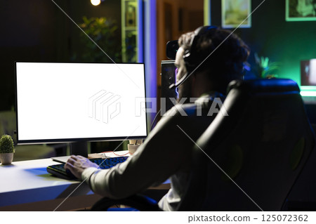 Man having fun by using isolated screen computer monitor to play singleplayer videogame. Professional gamer using mockup PC desktop to complete levels in game, talking with friends though headphones 125072362