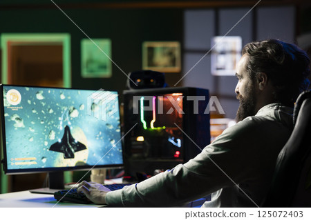 Happy man at home ready to relax by shooting asteroids in spaceship flying singleplayer game. Cheerful gamer sitting in gaming chair, navigating universe in simulation game Happy man at home ready to relax by shooting asteroids in spaceship flying singleplayer game. Cheerful gamer sitting in gaming chair, navigating universe in simulation game 125072403