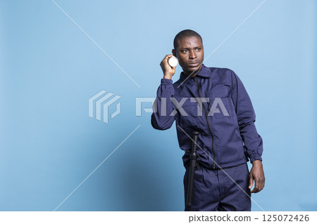 Male security agent using a flashlight for a night patrol in studio, inspecting the mall premises for protection. Bodyguard doing a control sweep in the dark, professional officer with a lantern. 125072426