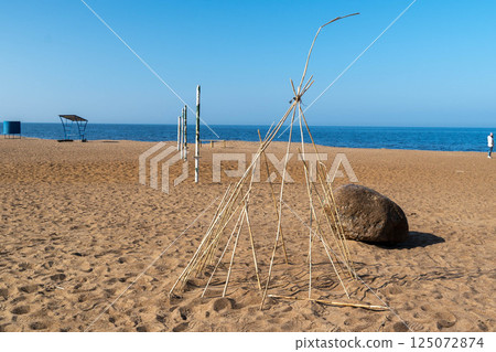Hut made of branches standing on sandy beach by sea Hut made of branches standing on sandy beach by sea 125072874