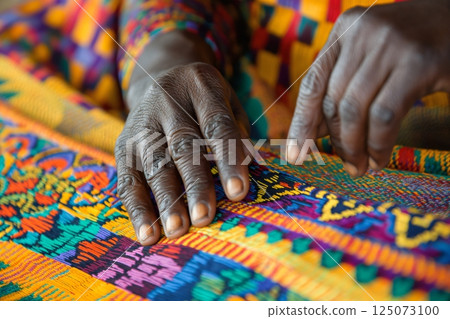 Close up of a textile worker carefully weaving colorful kente cloth using a traditional loom 125073100
