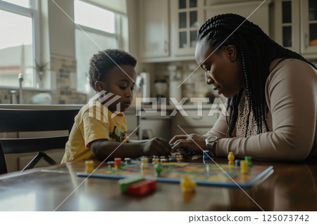 Mother and her young son are spending quality time together, playing a board game at their kitchen table Mother and her young son are spending quality time together, playing a board game at their kitchen table 125073742