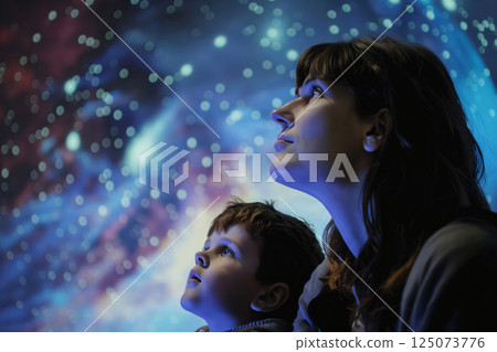 Mother and her son are enjoying a night out, gazing at the wonders of space in a planetarium 125073776