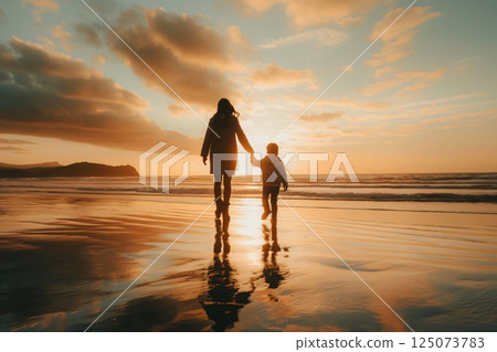 Mother and her son are silhouetted against a beautiful sunset as they walk hand in hand along a sandy beach Mother and her son are silhouetted against a beautiful sunset as they walk hand in hand along a sandy beach 125073783