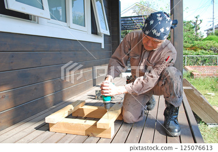 Carpentry: Man using power drill on deck Carpentry: Man using power drill on deck 125076613