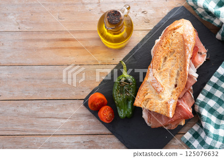 Spanish serrano ham sandwich on wooden table. Spanish bocadillo de jamon serrano. 125076632