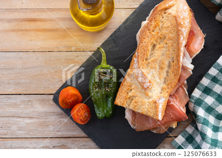 Spanish serrano ham sandwich on wooden table. Spanish bocadillo de jamon serrano. 125076633