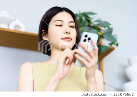 一位年輕女子在房間裡看著她的智慧型手機 一位年輕女子在房間裡看著她的智慧型手機 125076668