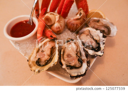 close up of seafood platter with raw oyster, crab legs, shrimps and escargots with cocktail sauce and lemon slice on the side. All on a bed of ice 125077339
