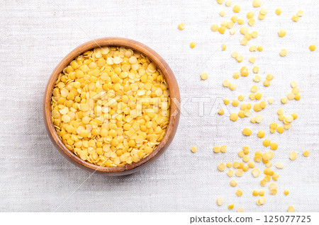 Yellow lentils in a wooden bowl on linen. Dried seeds of a Lens esculenta variety, a legume of small, round, and yellow fruits. High in protein and fiber, with soft and creamy texture, when cooked. Yellow lentils in a wooden bowl on linen. Dried seeds of a Lens esculenta variety, a legume of small, round, and yellow fruits. High in protein and fiber, with soft and creamy texture, when cooked. 125077725