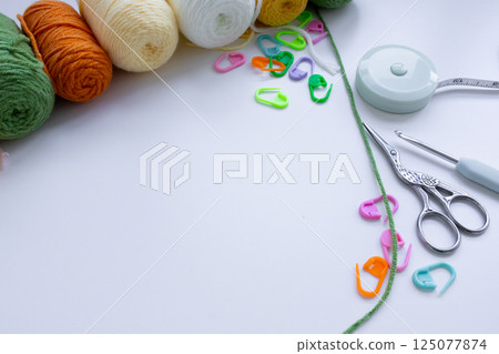 Colorful yarn balls with crochet tools and stitch markers on white surface Colorful yarn balls with crochet tools and stitch markers on white surface 125077874