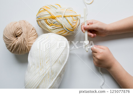Child crocheting with white yarn and multicolored wool balls 125077876