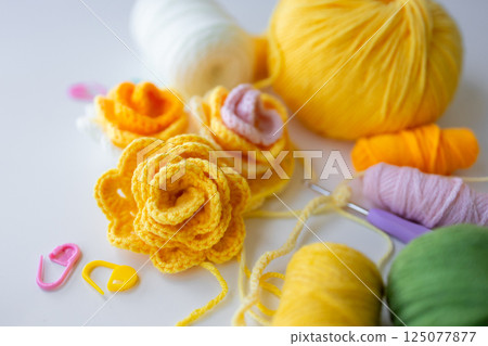 Colorful knit flowers with yarn and crochet hooks on white surface 125077877