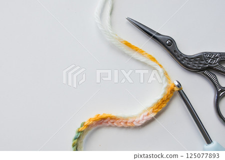 Crochet stitch pattern with colorful yarn, scissors, and hook on white background 125077893