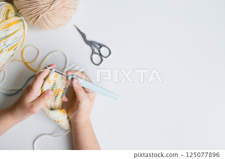 Child hands knitting with crochet hook and yarn on white background 125077896