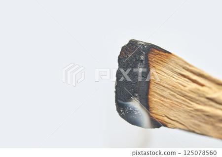 Close up of burned wooden matchstick with blackened tip and smoke against white 125078560