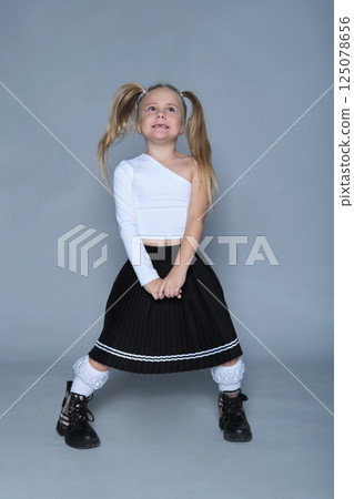 s little girl shows off her bold and joyful personality with a playful pose, making the most of the studio setting. Her trendy one-shoulder top and pleated skirt add a stylish flair to the energetic 125078656