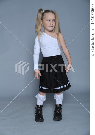A 5-year-old girl poses confidently in a stylish one-shoulder top and pleated skirt during a studio shoot, showing her potential in children's fashion. A 5-year-old girl poses confidently in a stylish one-shoulder top and pleated skirt during a studio shoot, showing her potential in children's fashion. 125078660