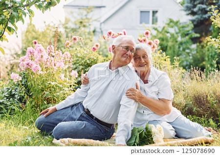 Sitting on the ground. Lovely senior couple is in the garden together Sitting on the ground. Lovely senior couple is in the garden together 125078690